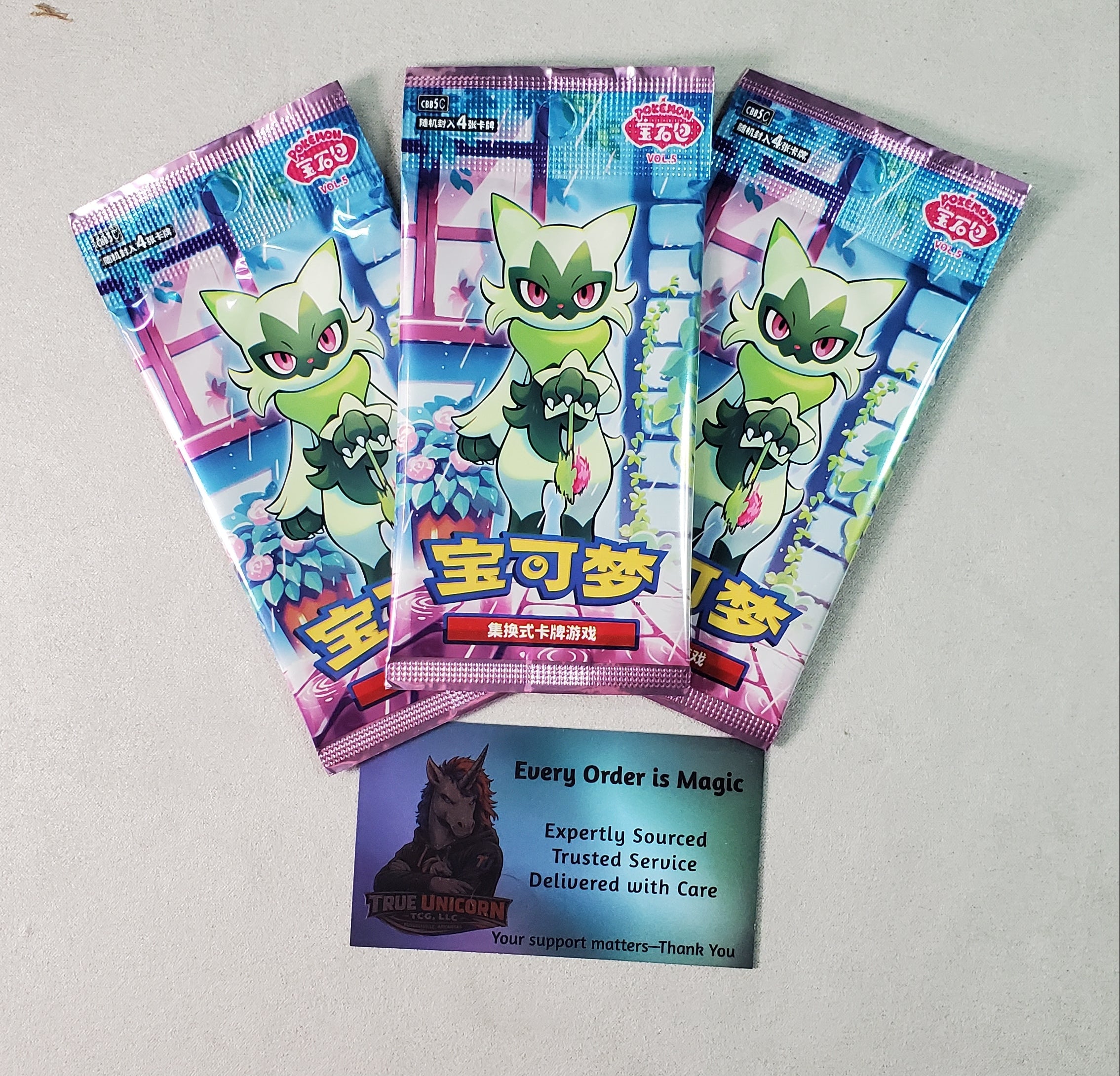 Three packs of Chinese Pokémon trading card booster packs are arranged on a white desk surface, with a keyboard visible at the bottom and a colorful card pack partially visible at the top.