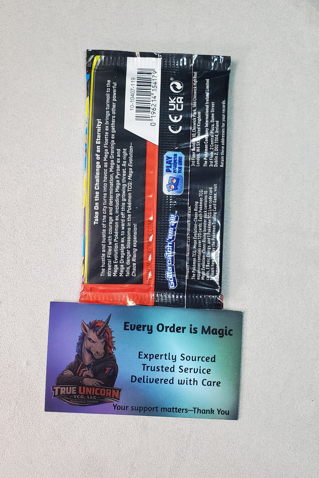 A sealed black product package with a barcode and small orange strip, placed above a printed card that reads 'Every Order is Magic' and 'True Unicorn,' on a light tabletop with a keyboard visible at the bottom.