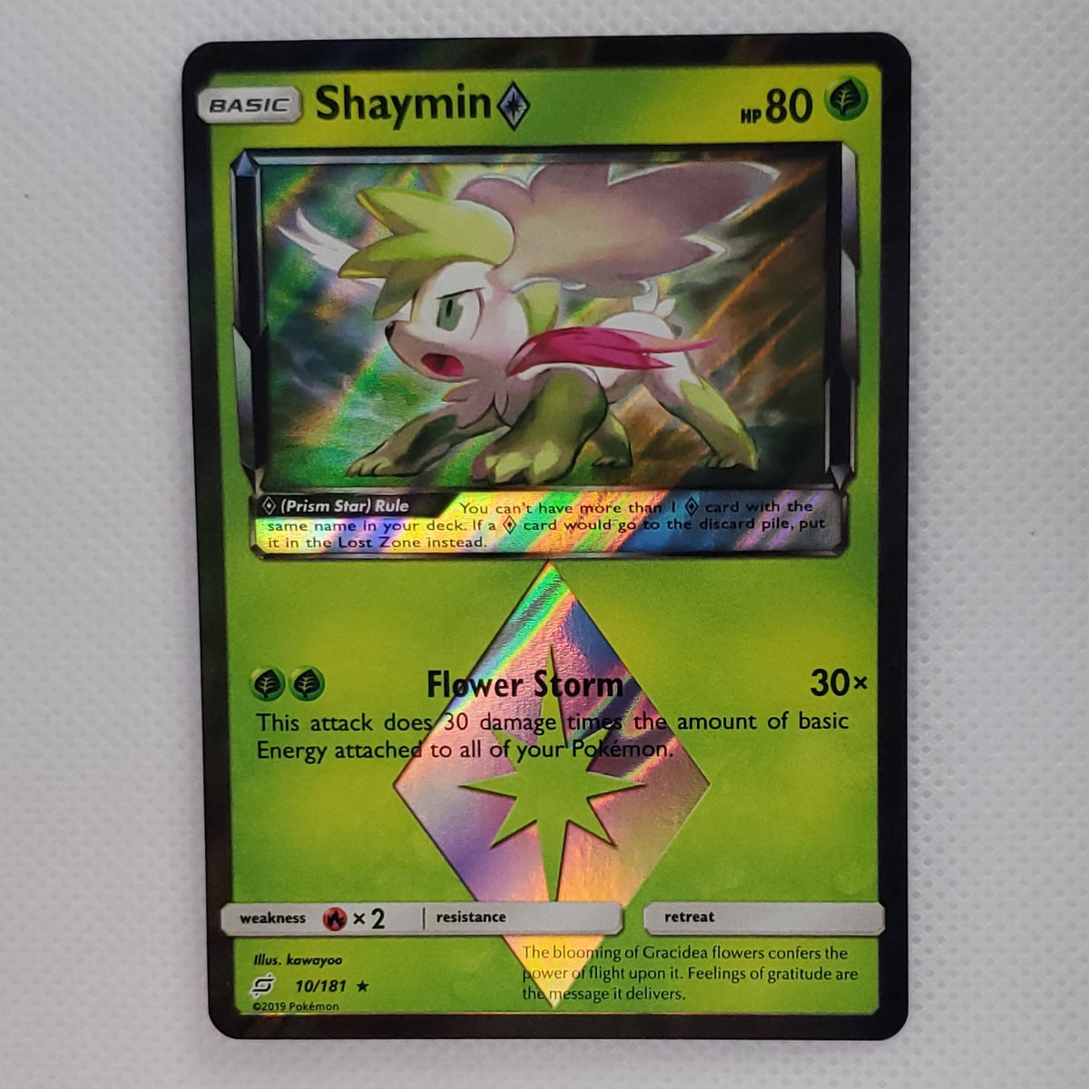 A single Pokémon trading card featuring Shaymin, displayed upright against a light gray backdrop with a small white display stand below.