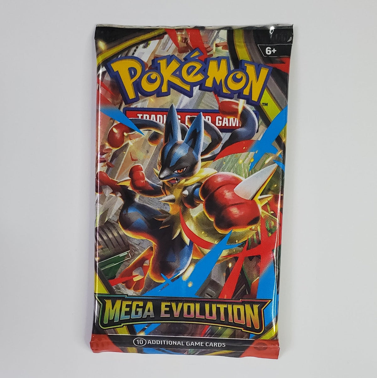 A sealed Pokémon TCG booster pack for 'Mega Evolution' stands upright against a plain white wall. The pack artwork features a dynamic illustration of a blue and red Pokémon character with the 'Pokémon' logo at the top and 'MEGA EVOLUTION' printed in large yellow text near the bottom.