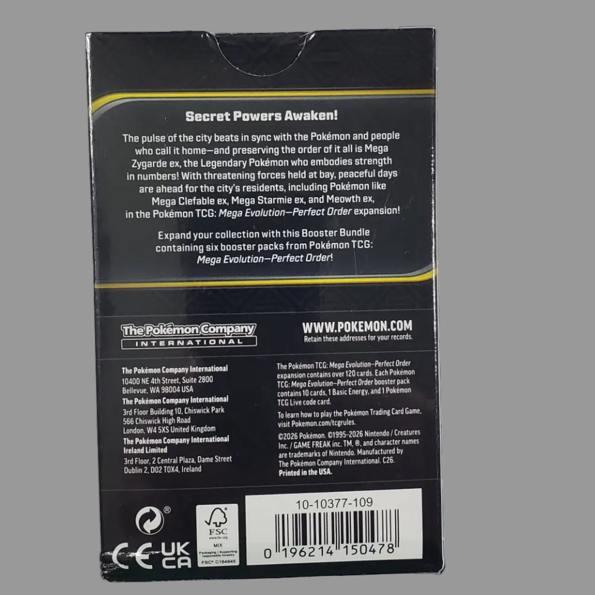 The back of a black product box with white text, a barcode, and small yellow accent lines, photographed on a white surface.