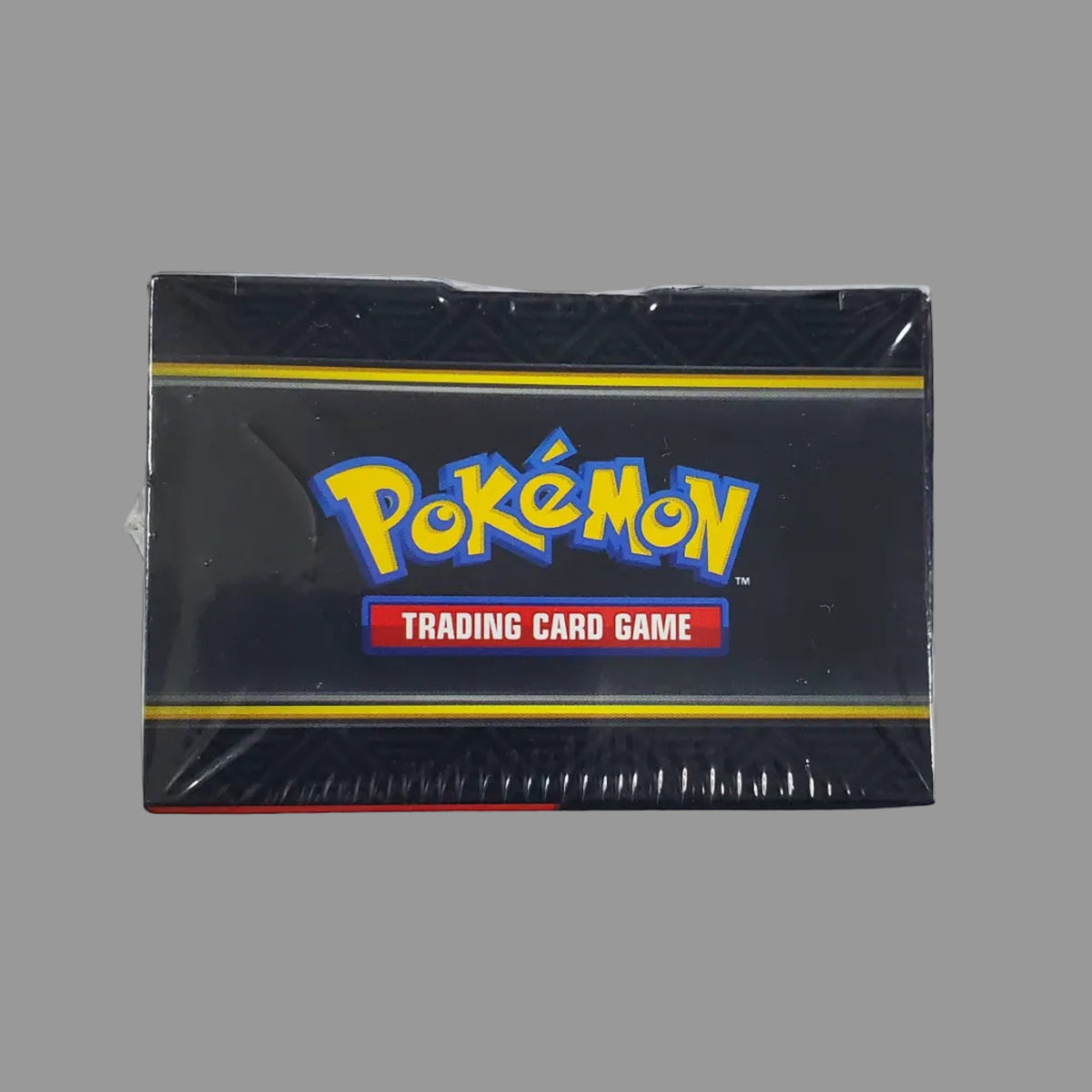A sealed black Pokémon Trading Card Game booster box centered on a white surface, with a keyboard and colorful background visible around it.