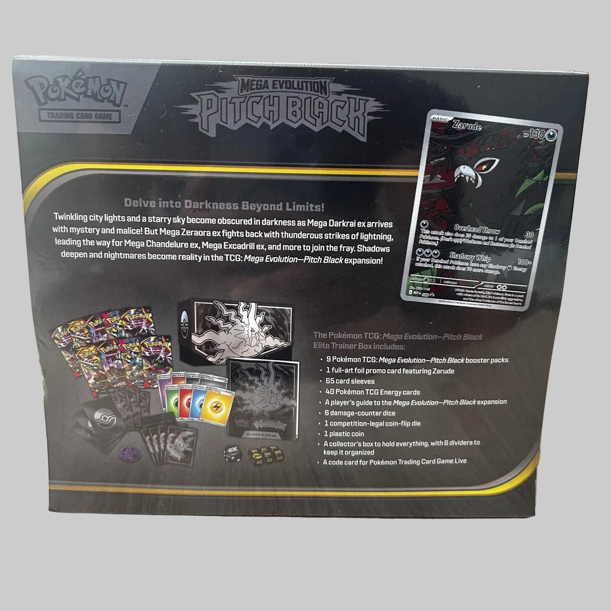 The back of a Pokémon TCG Mega Evolution Pitch Black Elite Trainer Box package, photographed on a wooden tabletop. The box shows product contents, rules text, a card example, and branding for Pokémon, Mega Evolution, and Pitch Black.