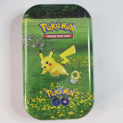 A rectangular metal tin with rounded corners featuring Pikachu on a green grassy field with yellow flowers. The top and bottom of the tin display the 'Pokémon Trading Card Game' logo, and the bottom features the 'Pokémon GO' logo.