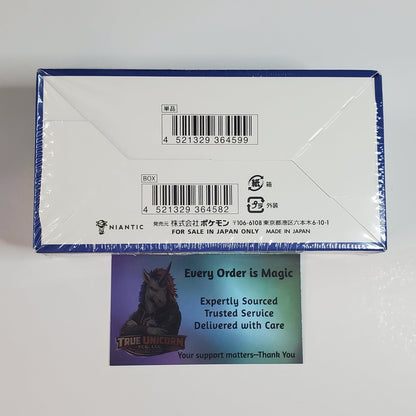 A sealed white product box with blue trim and printed barcodes, photographed on a plain light background. A small printed card with a horse illustration and the text 'Every Order is Magic' is placed in front of the box.