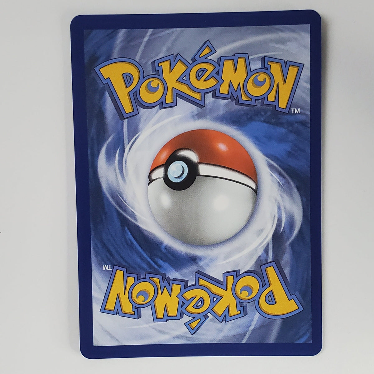 A Pokémon card featuring the classic blue background, yellow 'Pokémon' logo, and a red-and-white ball illustration, photographed against a white wall with a keyboard partially visible below.