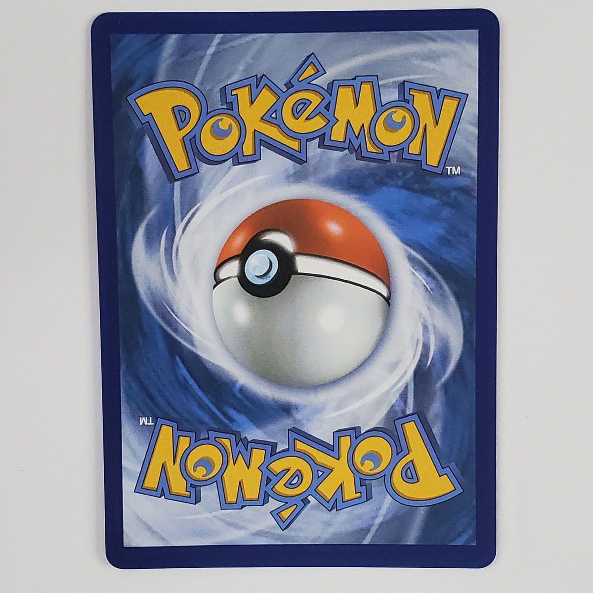 A Pokémon card featuring the classic blue back design with a large Pokémon Ball in the center and yellow 'Pokémon' text, photographed against a plain white wall.