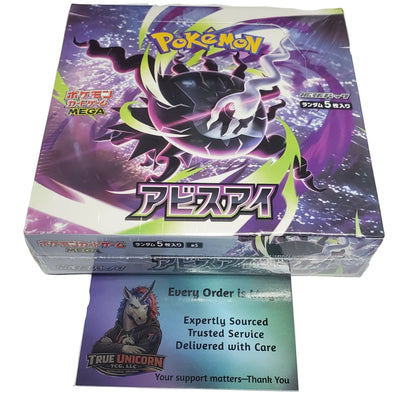 A Pokémon TCG booster box with Japanese text, featuring a purple and black design with the character Artisan. A 'True Unicorn' \ card is placed in front of the box on a white desk.