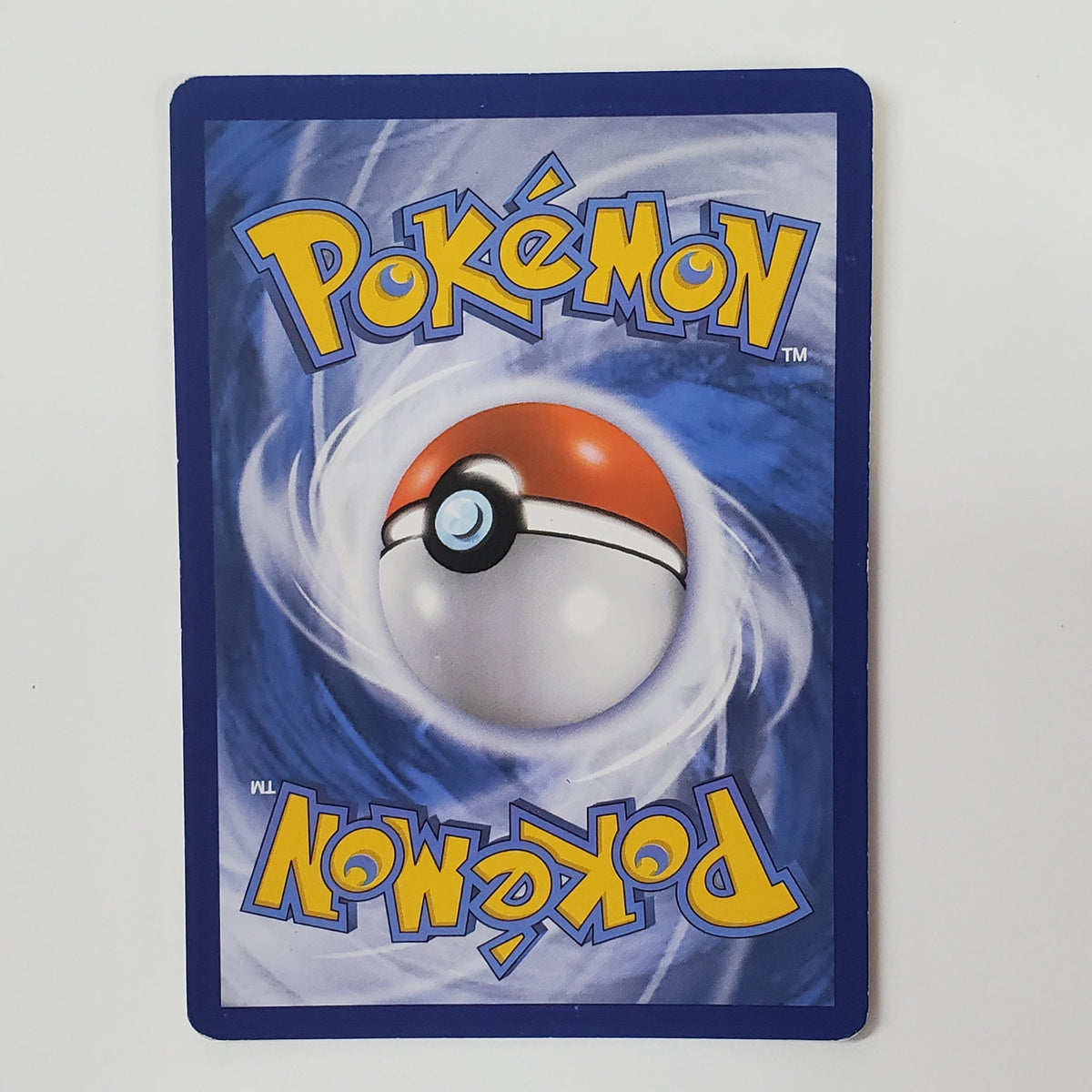 A Pokémon trading card featuring the classic blue background, yellow 'Pokémon' logo, and a red-and-white ball illustration, photographed against a white wall above a desk.