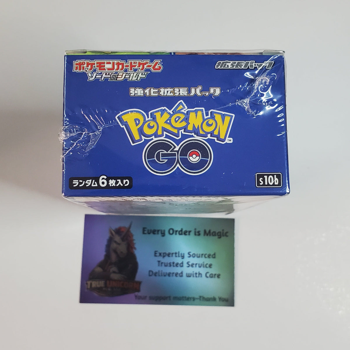 A blue Pokémon GO trading card booster box on a white surface, with a small card in front that reads 'Every Order is Magic' and 'Expertly Sourced Trusted Service Delivered with Care.'.