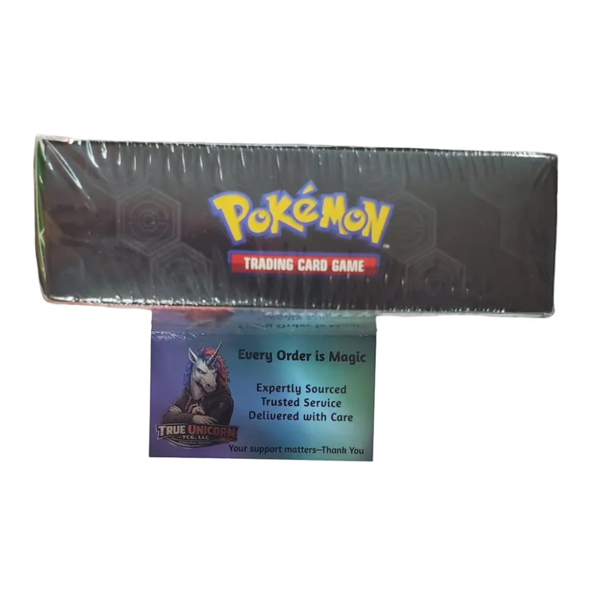 A sealed Pokémon Trading Card Game box is mounted on a white wall above a colorful Pokémon-themed display or shelf. A Pokémon card is visible in front of the box.