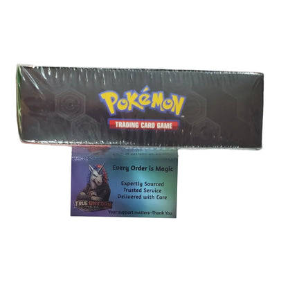 A sealed Pokémon Trading Card Game box is mounted on a white wall above a colorful Pokémon-themed display or shelf. A Pokémon card is visible in front of the box.