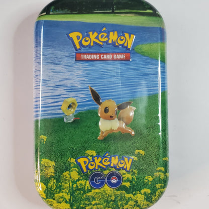 A rectangular metal Pokémon Trading Card Game tin with rounded corners, featuring artwork of Eevee by a lake with yellow flowers at the bottom and the Pokémon logo at the top.