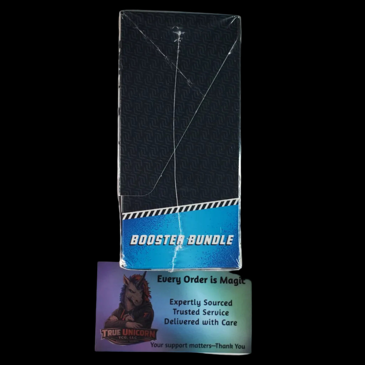 A sealed black rectangular product box with a blue band reading 'BOOSTER BUNDLE' stands on a white surface, with a small card underneath showing the True Unicorn logo and support text.